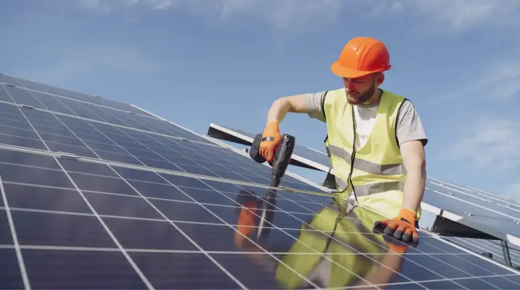 Technician installing solar panels on a roof with power drill.